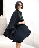 Woman wearing a Knitted Cashmere Cape in Black with ruffles, with sunglasses in an urban setting