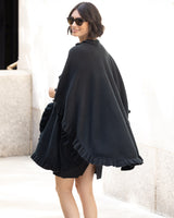 Woman wearing a Knitted Cashmere Cape in Black with ruffles, in an outdoor setting