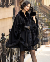 Woman wearing a Cervinia fur trimmed cashmere cape coat in black standing on a city street.