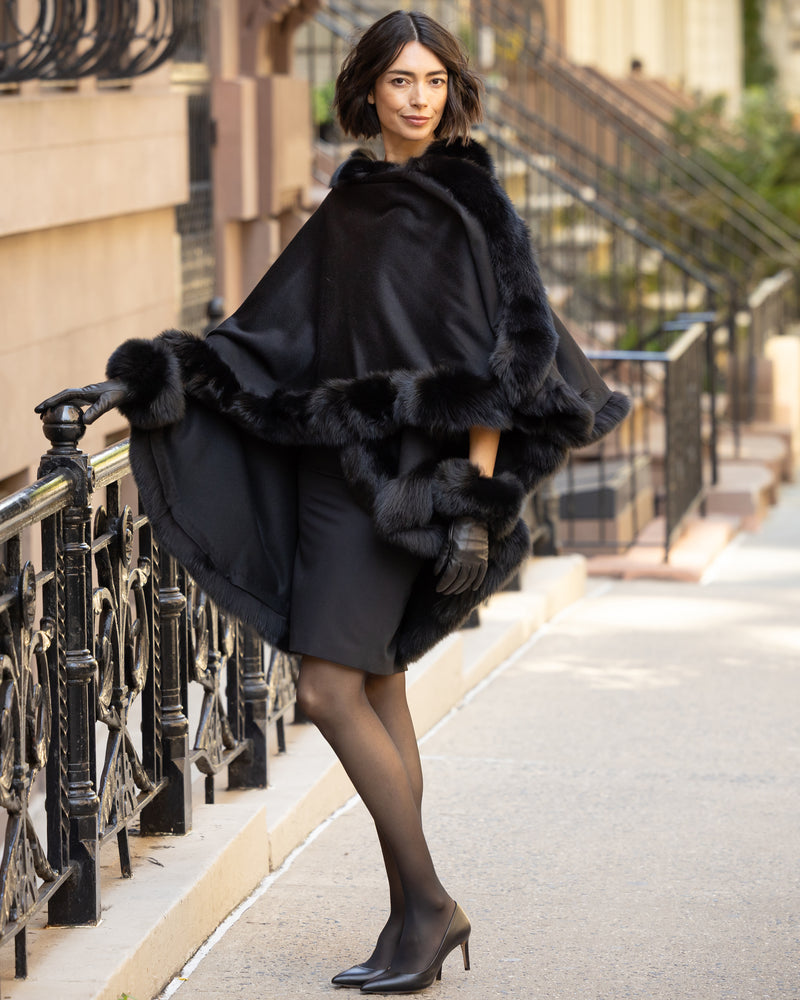 Woman wearing a Cervinia fur trimmed cashmere cape in black and fur trimmed  leather gloves on a city street.