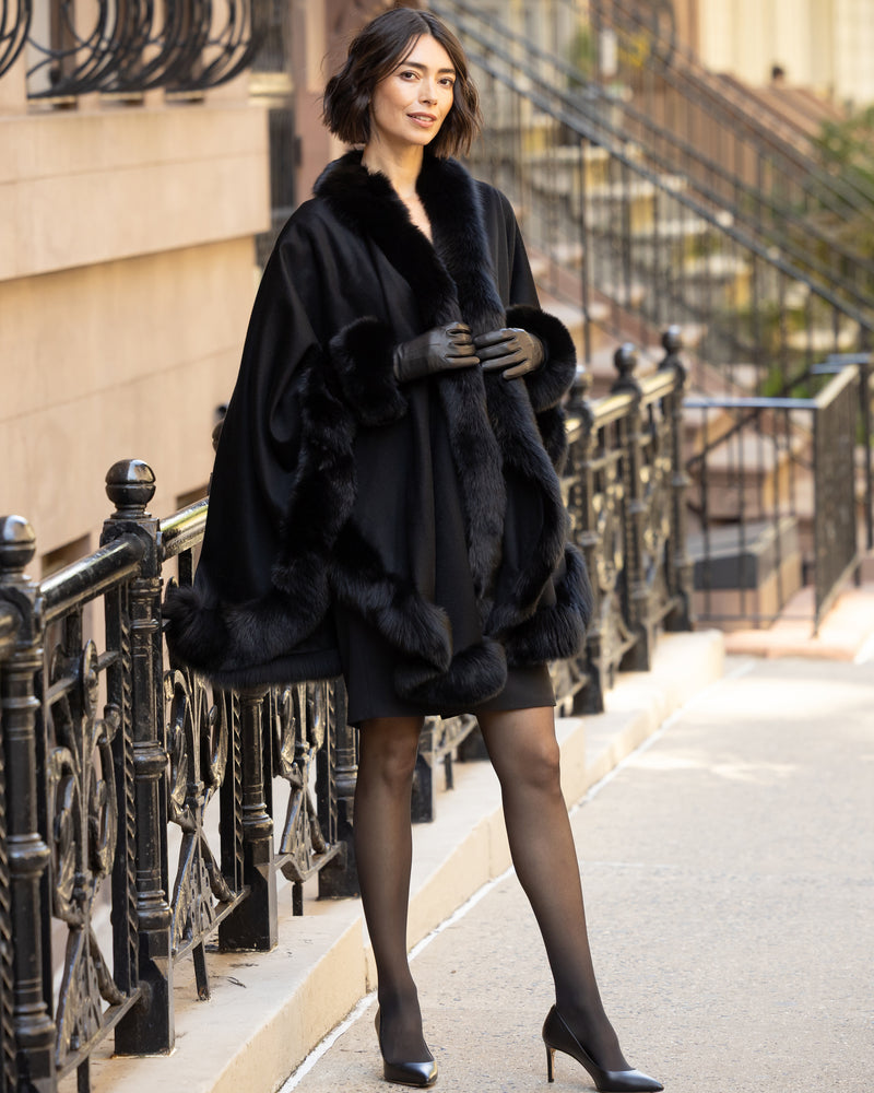 Woman wearing a fur trimmed cashmere cape in black on a city street.