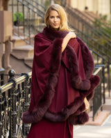 Woman wearing a fur trimmed cashmere cape in burgundy in an urban setting