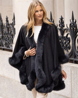 Woman wearing a Fur Trimmed cashmere Cape in Charcoal standing in front of decorative railings.