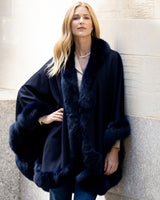 Woman wearing a cervinia fur trimmed cashmere cape against a wall.