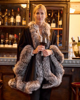 Woman wearing black multi silver fur trimmed cervinia standing in front of a bar holding a glass of wine
