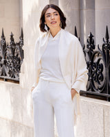 Woman wearing Cashmere water weave wrap with fringe in ivory standing in front of a decorative metal railing and wall.