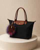 Black Tri-Color pom keychain on a black bag on a platform
