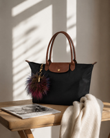 Black Tri-Color pom keychain on a black bag on a desk