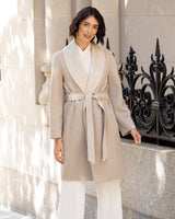 Woman wearing a Gabriella cashmere wrap coat with belt in Oat/Beige standing in front of a decorative metal railing.