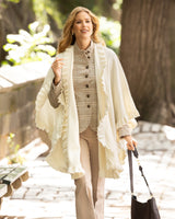 Woman walking outdoors wearing a Knitted Cashmere Cape with ruffles in Ivory and carrying a handbag.