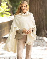 Woman wearing a Knitted Cashmere ruffled Cape in Ivory with ruffles in a city sidewalk setting
