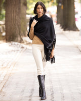 Woman wearing Cashmere Wrap with Leather Fringe in black, beige sweater, white pants, and black boots on a street.