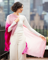 Woman wearing a Lightweight Cashmere Wrap in pink ombre with a blurred cityscape background
