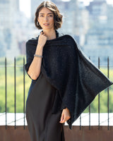 Woman wearing Radiant Cashmere Sequin Wrap in black against a cityscape background