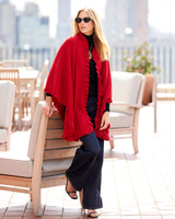 Woman on rooftop wearing sunglasses and volant knit cape in red, leaning against a chair