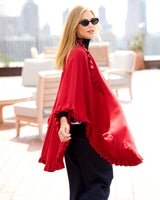 Woman on rooftop wearing sunglasses and volant knit cape in red, side view