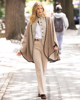 Woman walking outdoors wearing a Reversible Cashmere Cape with Leather trim in Oat/Beige, blouse, and trouser pants.