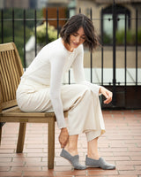 Woman in a monochromatic outfit sitting on a wooden bench outdoors wearing cashmere slippers in grey