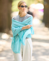 A woman standing outdoors in a park-like setting, wearing a turquoise wrap or shawl draped over shoulders.