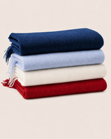 Stack of four folded cashmere blankets in powder blue and other colors on a beige background