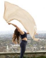 Woman in yoga outfit tossing up Voyage Cashmere Travel Wrap in oatmeal in the air with city skyline in background